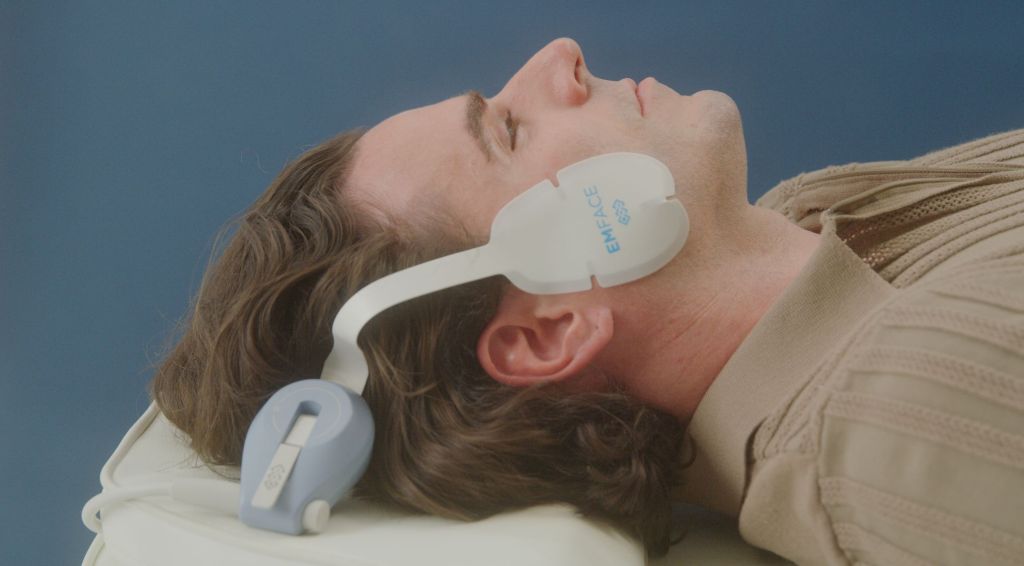 EMFACE Treatment - man laying on a clinical table with the device treating his jaw area.